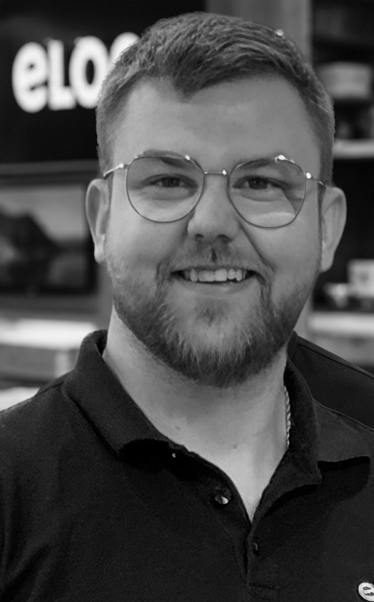 Smiling man with short hair and a beard wearing round glasses in a store setting.
